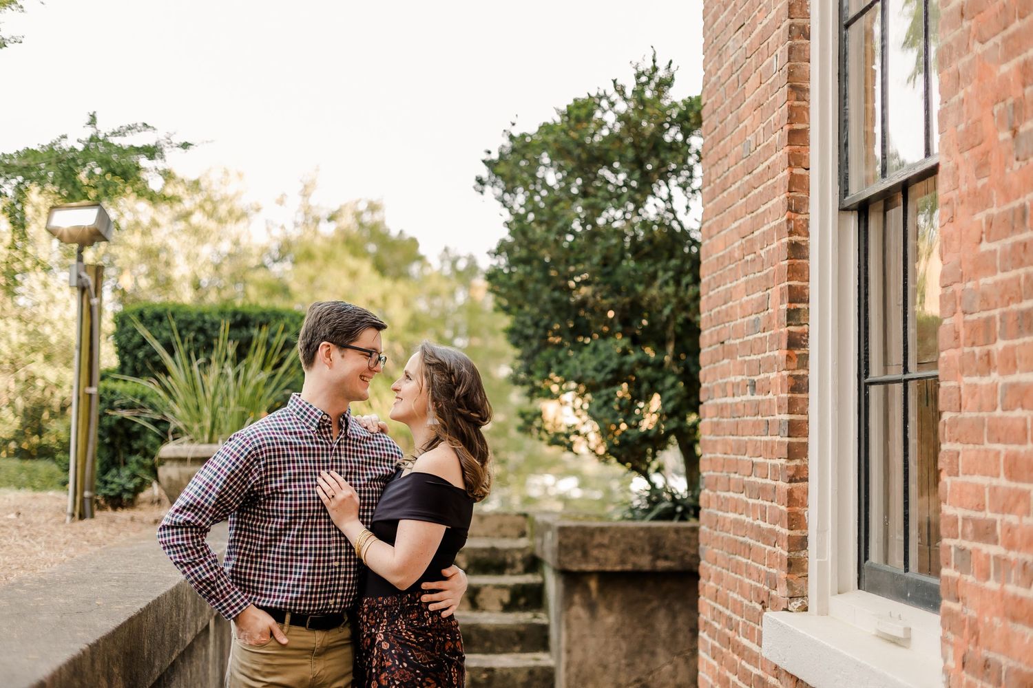 Couple poses for engagement photos against rustic brick building exterior.