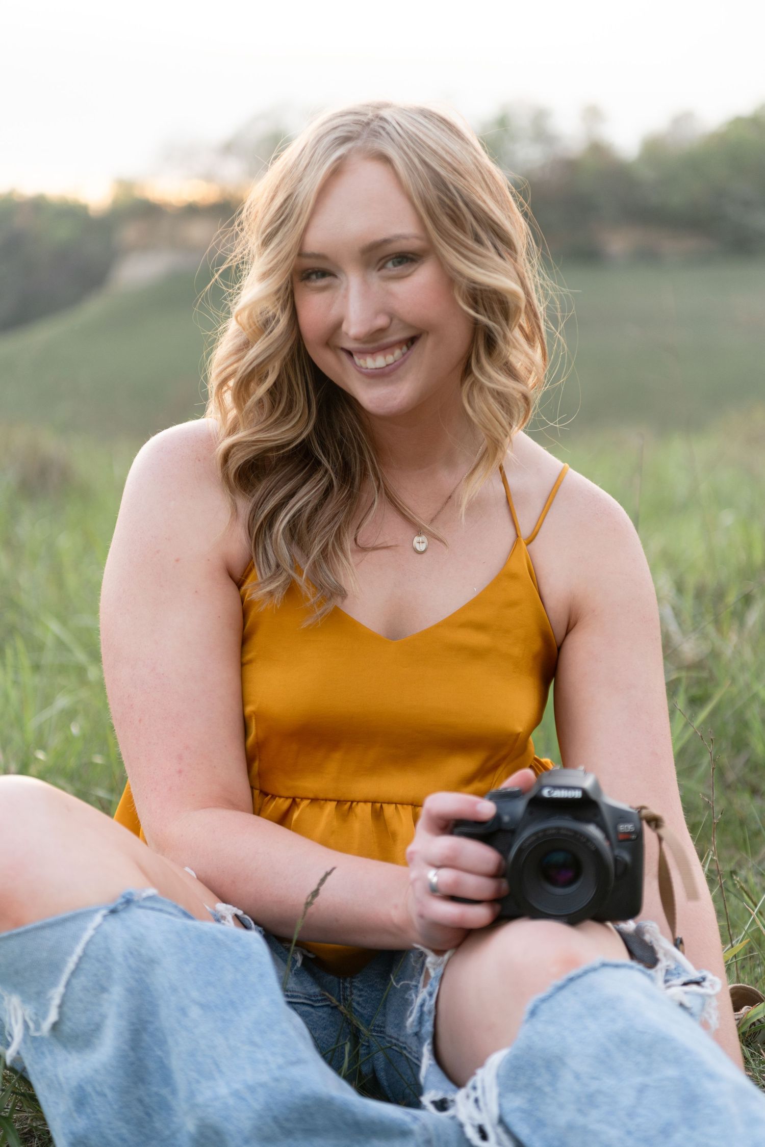 Person in yellow dress sits in grassy field holding professional camera.