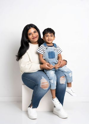 A pair sitting together on a white stool wearing matching white sneakers, ripped jeans and casual tops against a light background.