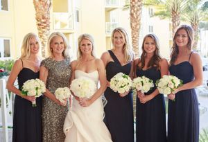 Bride in ivory gown poses with bridesmaids in navy dresses holding white bouquets.