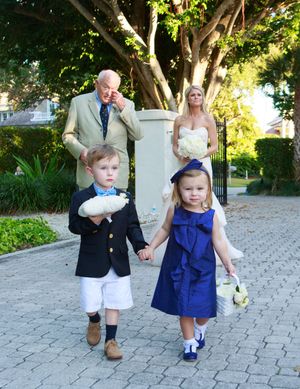 Ring bearer and flower girl lead bride and elder man down cobblestone path. Naples