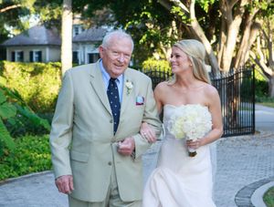 Bride in strapless white gown walks with elderly gentleman on garden pathway. Naples