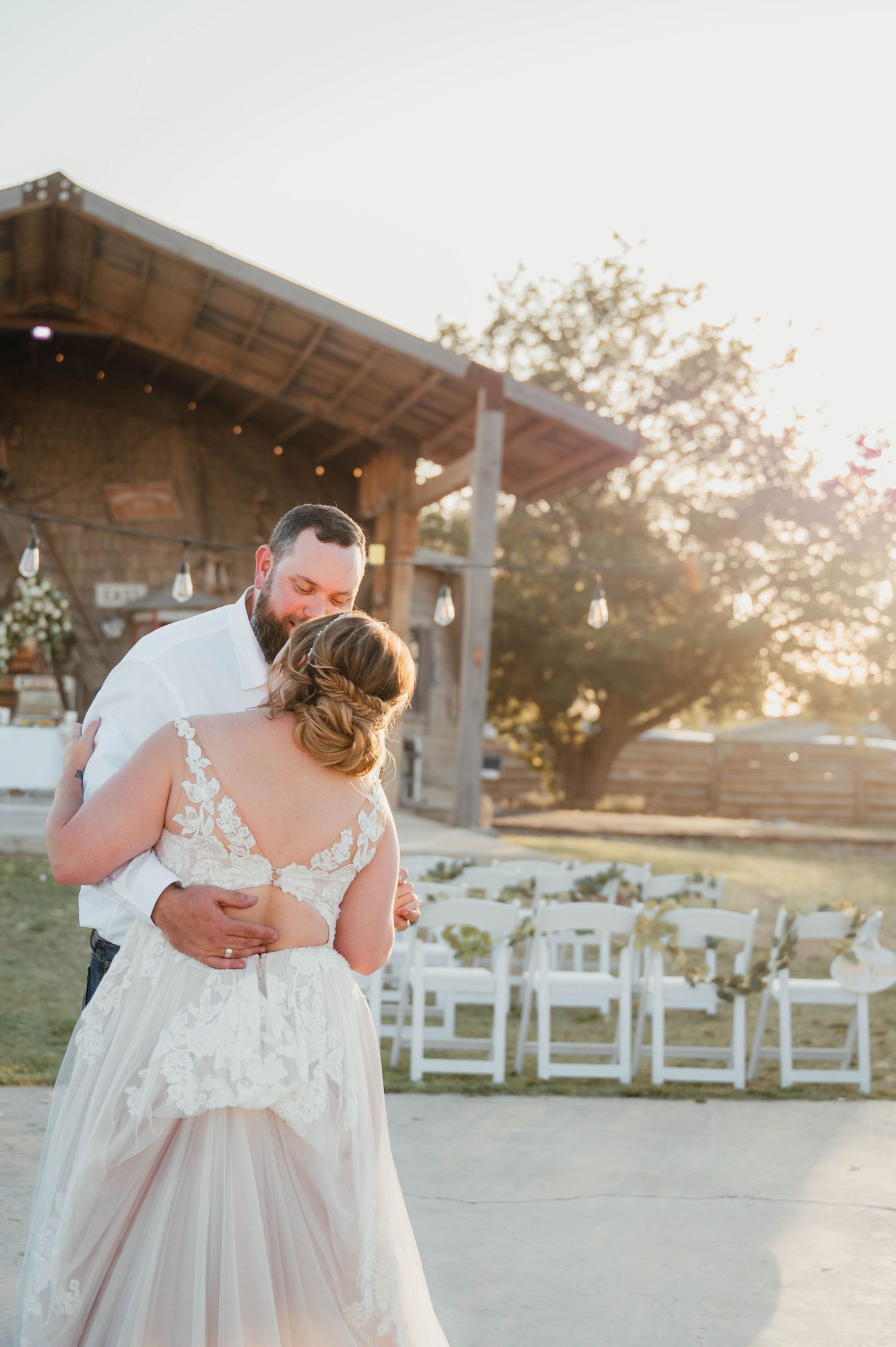 A couple shares an intimate dance moment at their outdoor wedding reception with white chairs in the background.