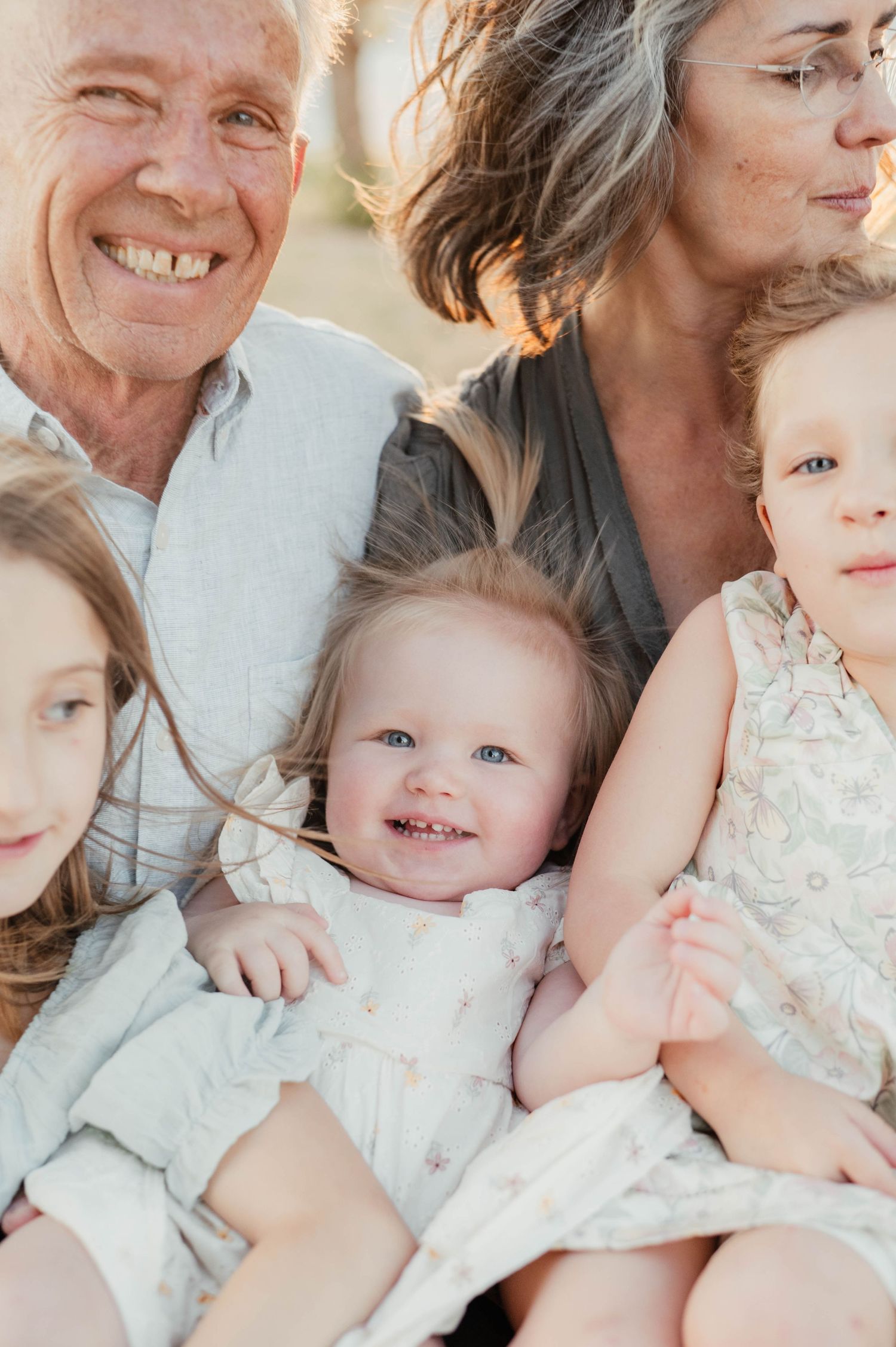 A multi-generational family poses together for a warm sunset portrait in light colored clothing.