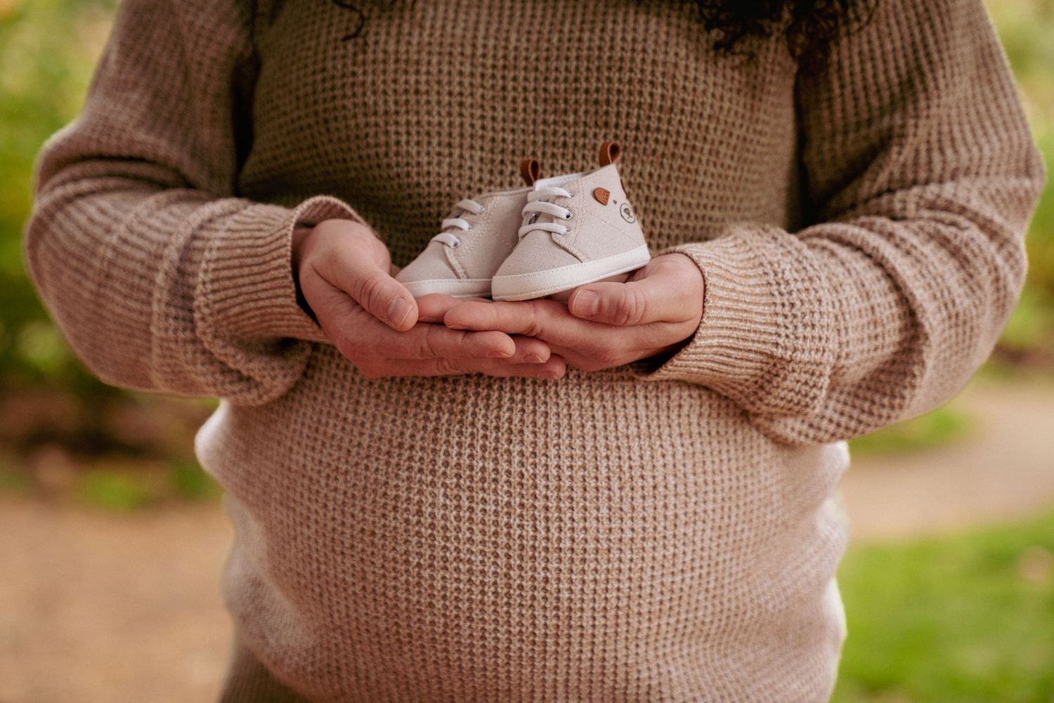 Close-up of hands holding baby shoes on baby bump, soft sweater texture, cozy PNW maternity photo.