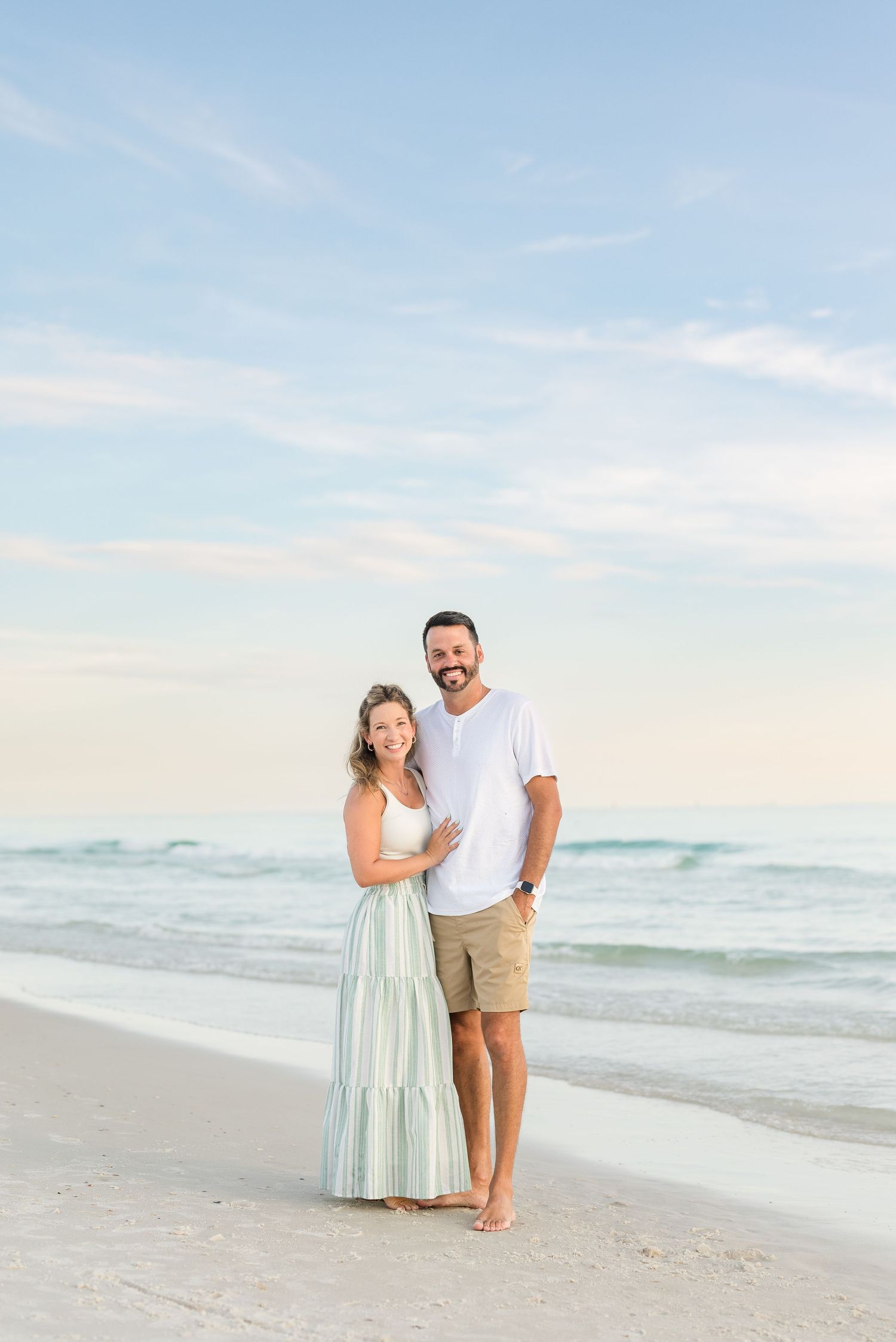 Couple embracing on a sandy beach beside the ocean during a romantic sunset portrait session.