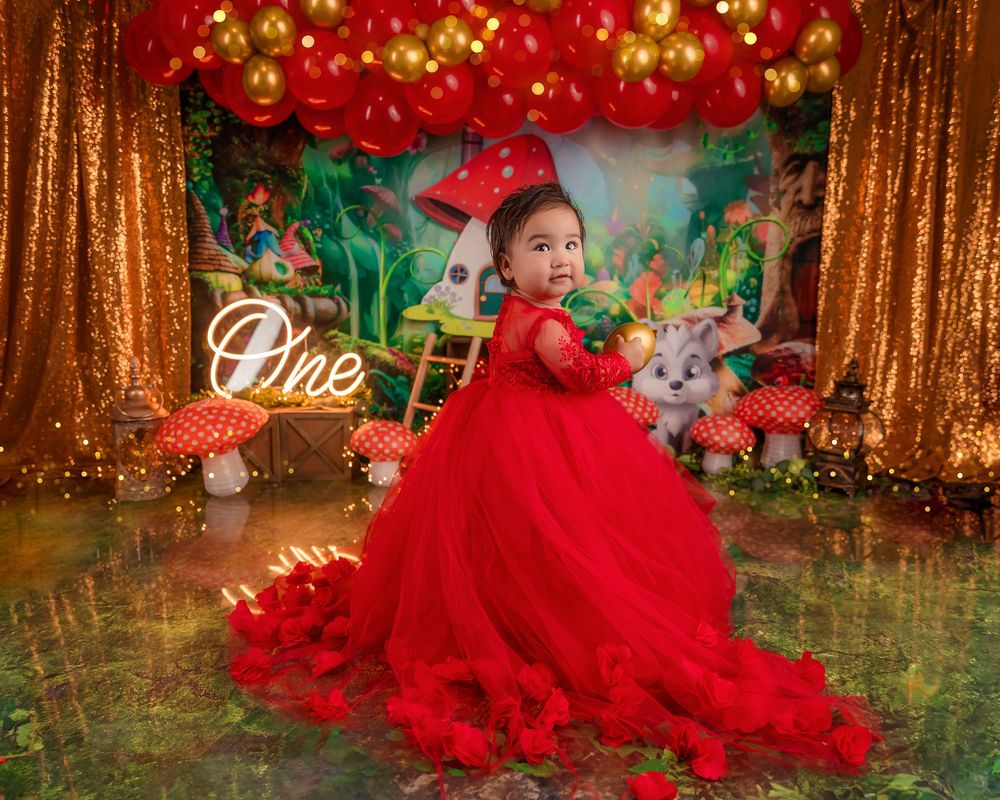 Little girl in red tulle gown poses at Alice in Wonderland mushroom-themed first birthday party celebration.