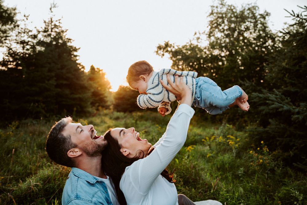 Parents lifting child playfully in air during outdoor family photoshoot at sunset.