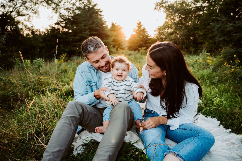 Family sitting together on blanket sharing laughs during outdoor photo session.