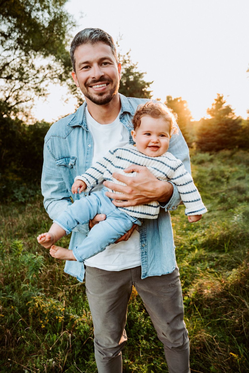 Parent holding child wearing striped sweater during outdoor sunset photoshoot.