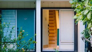 Colorful home entrance with teal blue door, number 75, wooden staircase visible through open doorway, and lush green plants.