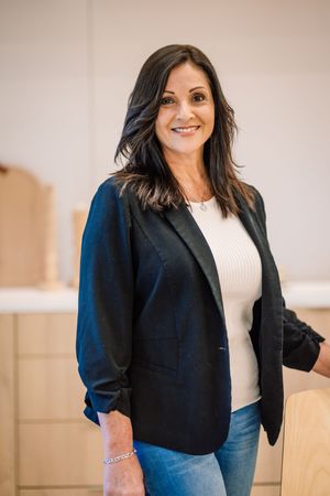 Professional woman in black blazer and jeans smiling confidently in a modern office setting.
