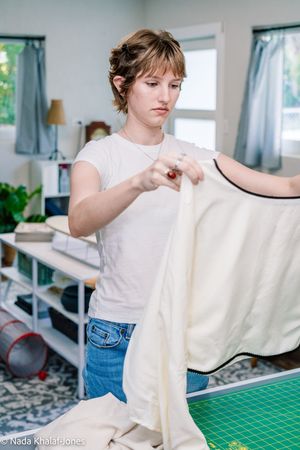 Young woman in white t-shirt and jeans working with cream fabric in a bright sewing studio.