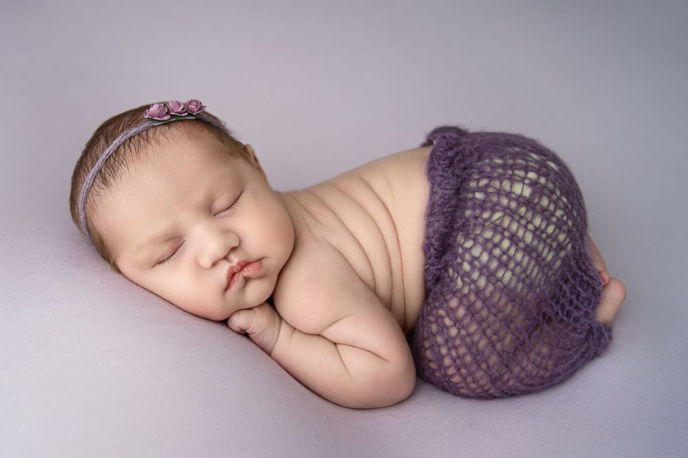 Artistic newborn photo with purple knit wrap on soft gray background.