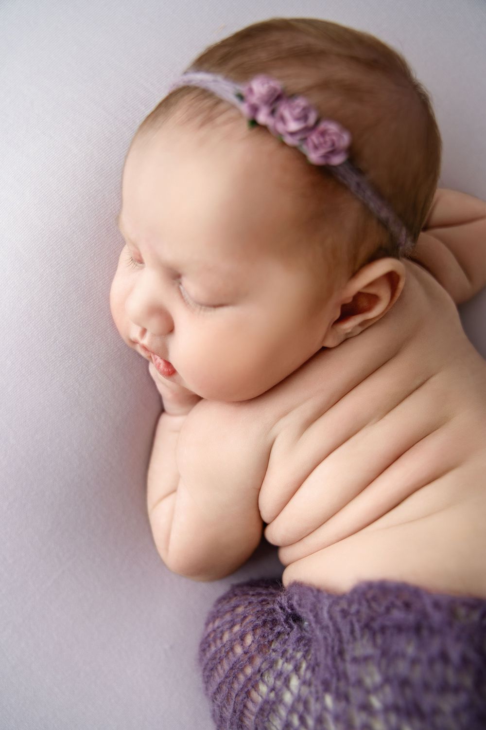 Delicate newborn portrait with purple floral headband and knit wrap.