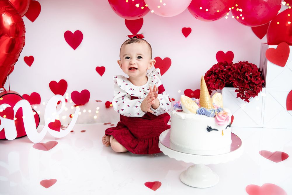 Valentine's day themed cake smash setup with red hearts, balloons and white cake.