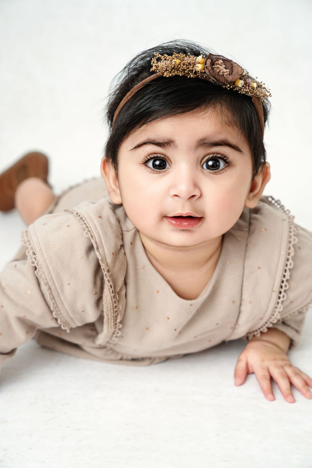 Baby in neutral colored outfit lying on white studio background.