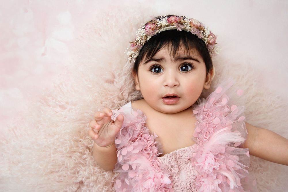 Baby wearing pink tulle dress and floral headband in studio portrait.