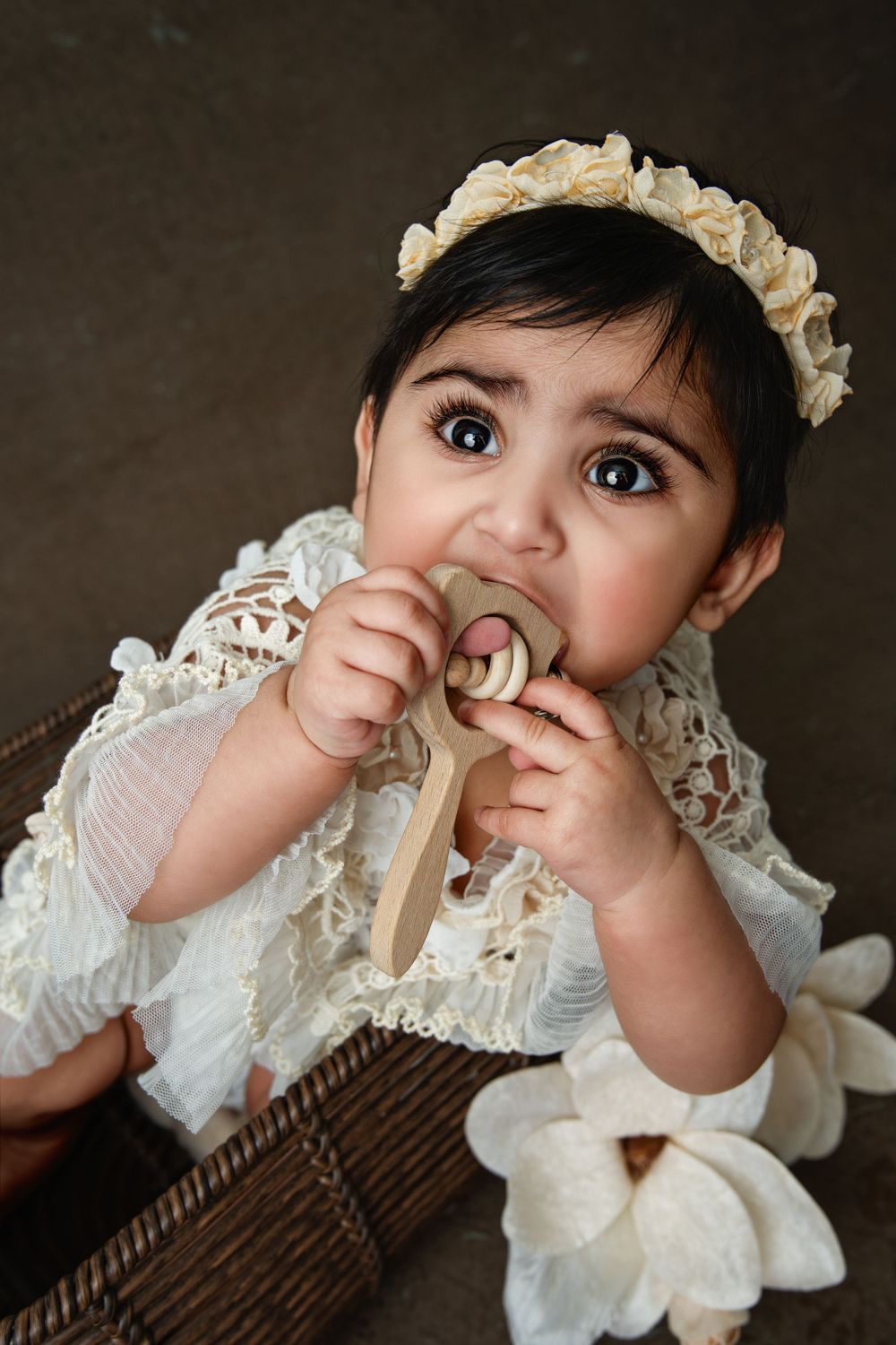 Baby in vintage white lace dress and floral crown during professional photo shoot.