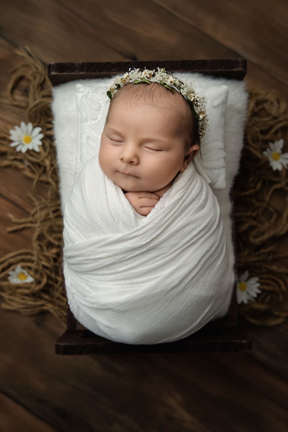 Newborn photography with white wrap and floral crown on wooden backdrop with daisies.