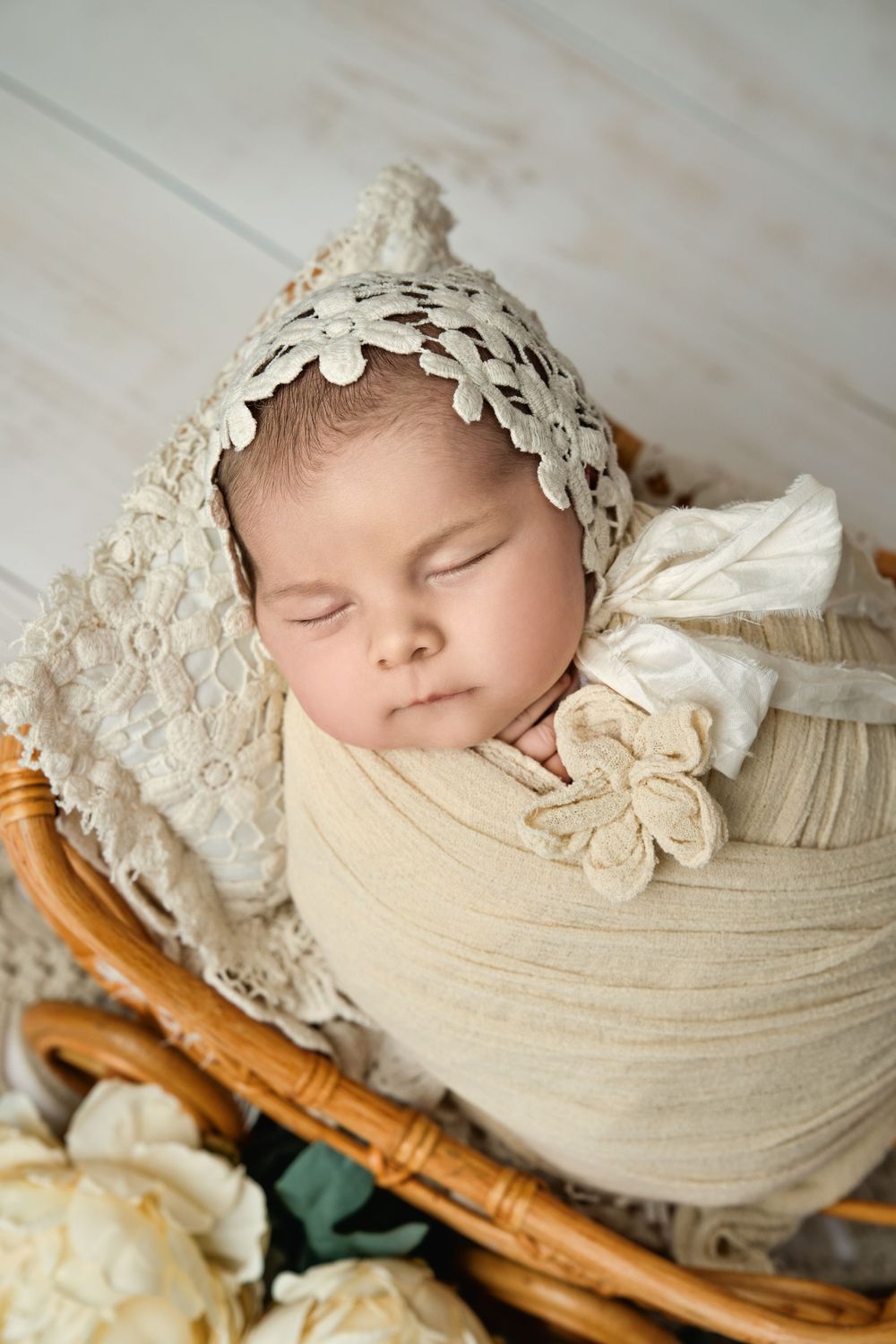 Vintage-style newborn portrait with cream lace bonnet and wrap in antique basket.