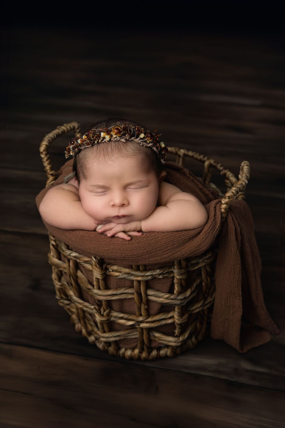 Artistic newborn photography in woven basket with brown tones and moody lighting.