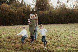 Family enjoying a playful moment together in a grassy field with trees in the background.