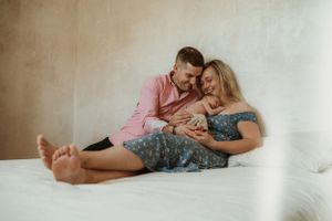 Intimate family moment on white bedding as couple gazes at their newborn.