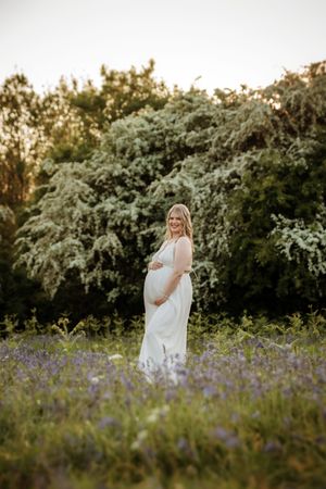 Ethereal maternity photoshoot in a field of purple wildflowers during golden hour.