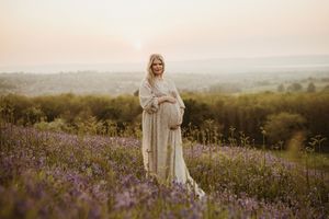 Scenic maternity session overlooking rolling hills at sunset with flowing white dress.