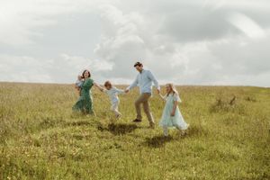 Family playing together on grassy hillside during golden hour photoshoot.