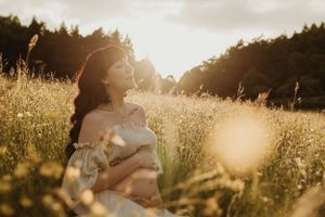A dreamy golden hour portrait in a sunlit meadow with tall grass and forest backdrop.