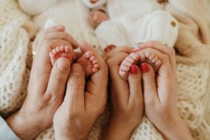 Close-up of tiny baby feet being held gently in adult hands on a knit blanket.