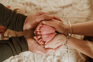 Gentle hands holding and caressing tiny newborn baby feet.
