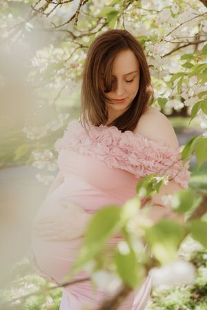 Dreamy spring maternity portrait under blooming cherry blossoms with pink floral dress.