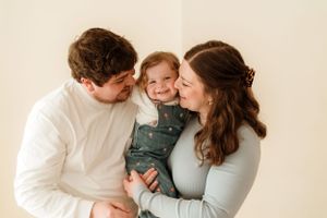 A tender family moment captured in soft natural light against a neutral background.