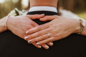 Close-up of hands with wedding rings embracing from behind.