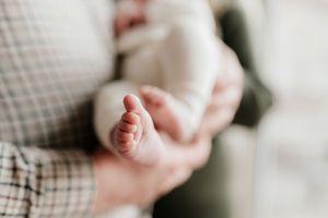 Close-up view of a newborn baby's tiny feet and hands against a soft white background by Pausing time Photography