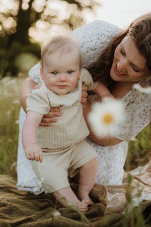 Sweet candid moment with baby in cream knit outfit among blooming daisies.