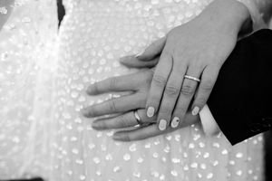 A close-up photo of hands showing wedding rings against a white textured background.