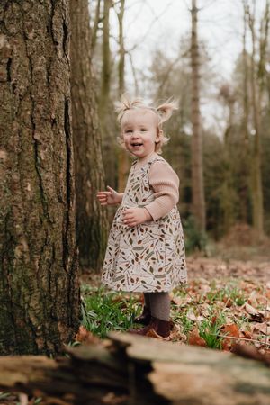 A series of photos showing a small child playing among fallen leaves and early spring flowers in a wooded forest setting in Cheltenham