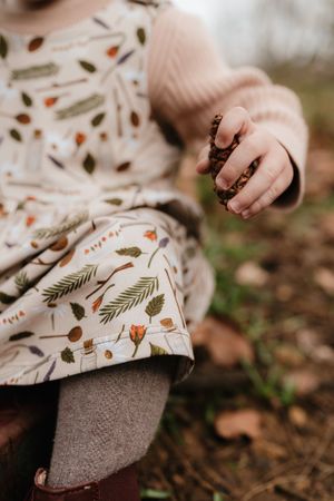 Close-up view of hands in a floral printed dress touching autumn leaves scattered on brown earth.