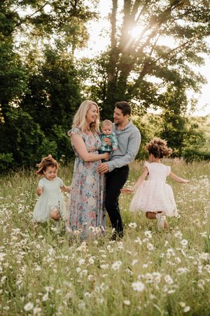 A joyful family moment captured in a wildflower meadow at golden hour with sunlight streaming through trees.
