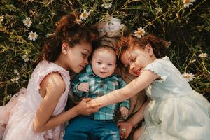 Intimate family portrait with children cuddling together in a meadow setting.