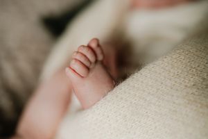 Close-up of a newborn baby's tiny hand and feet wrapped in a soft cream knit blanket.