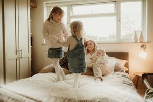 Family bonding moment on white bedding in sunlit bedroom.
