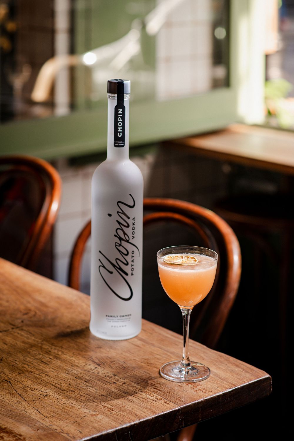 White bottle and orange cocktail on rustic wooden table in warm ambient lighting.