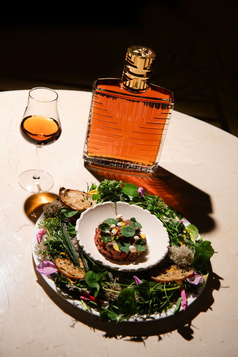 Gourmet seafood dish plated with greens and garnishes alongside decorative bottles.