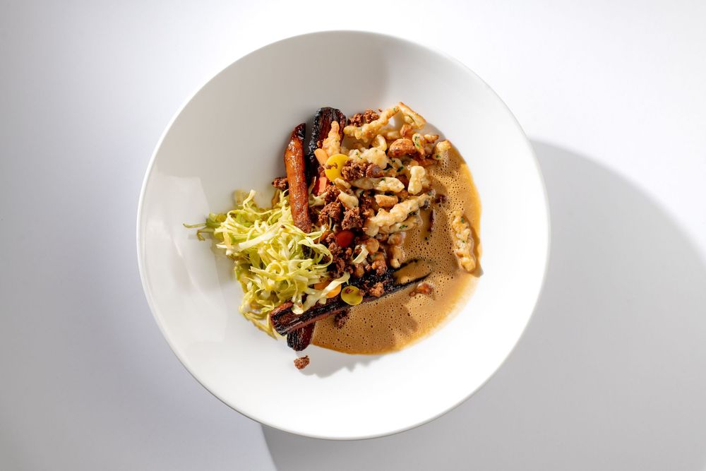 A plated fine dining dish with garnishes and sauces presented in an elegant white bowl on a light background.