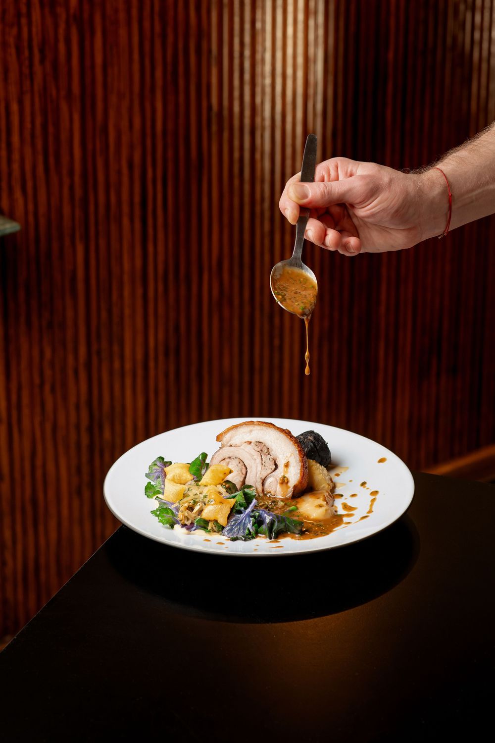 Sauce being drizzled onto a plated dish in a dramatic lighting setup against a dark wooden background.